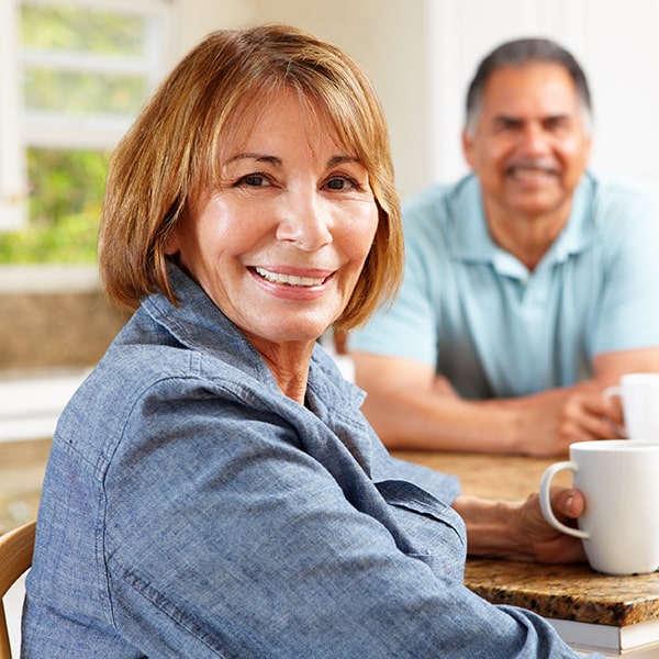 An older couple sitting at the table smiling and drinking coffee