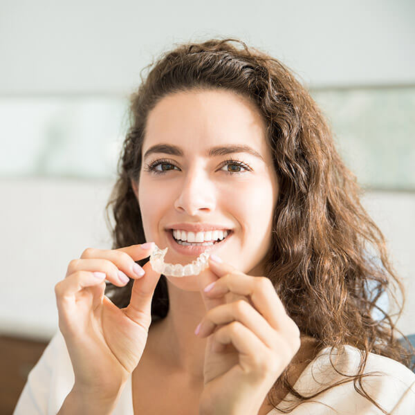 Woman smiling and holding her Invisalign aligner