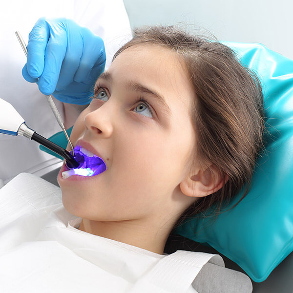 Young girl sitting in the dentist chair with the mouth open while the dentist works.