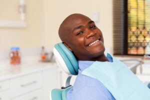 A bald Black man smiles as he leans back in a dental chair while waiting for his dental checkup