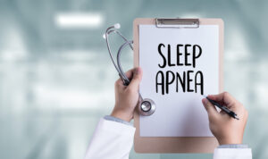 A dentist holds a stethoscope and a clipboard with a paper after writing SLEEP APNEA with a black pen